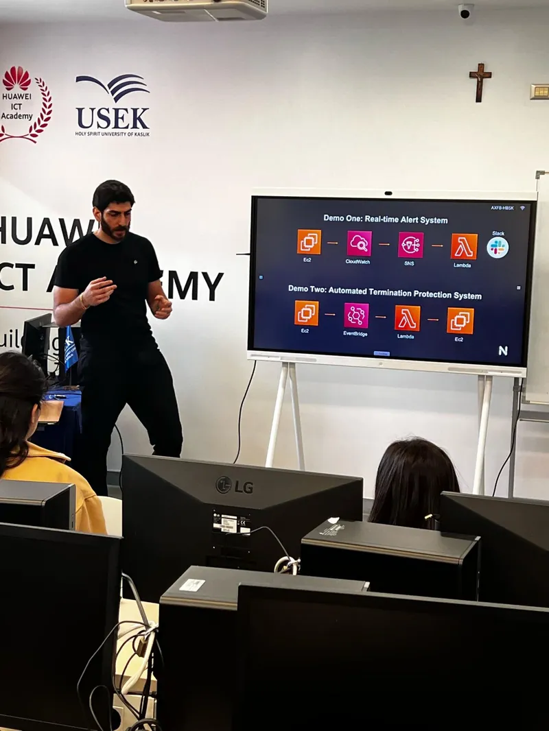 The same AWS demo seen from behind the lab computers, Elio presenting beside the screen.