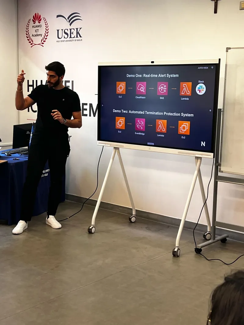 Elio explaining two AWS demos on a screen, a real-time alert system and automated termination protection, at the Huawei ICT Academy at USEK.